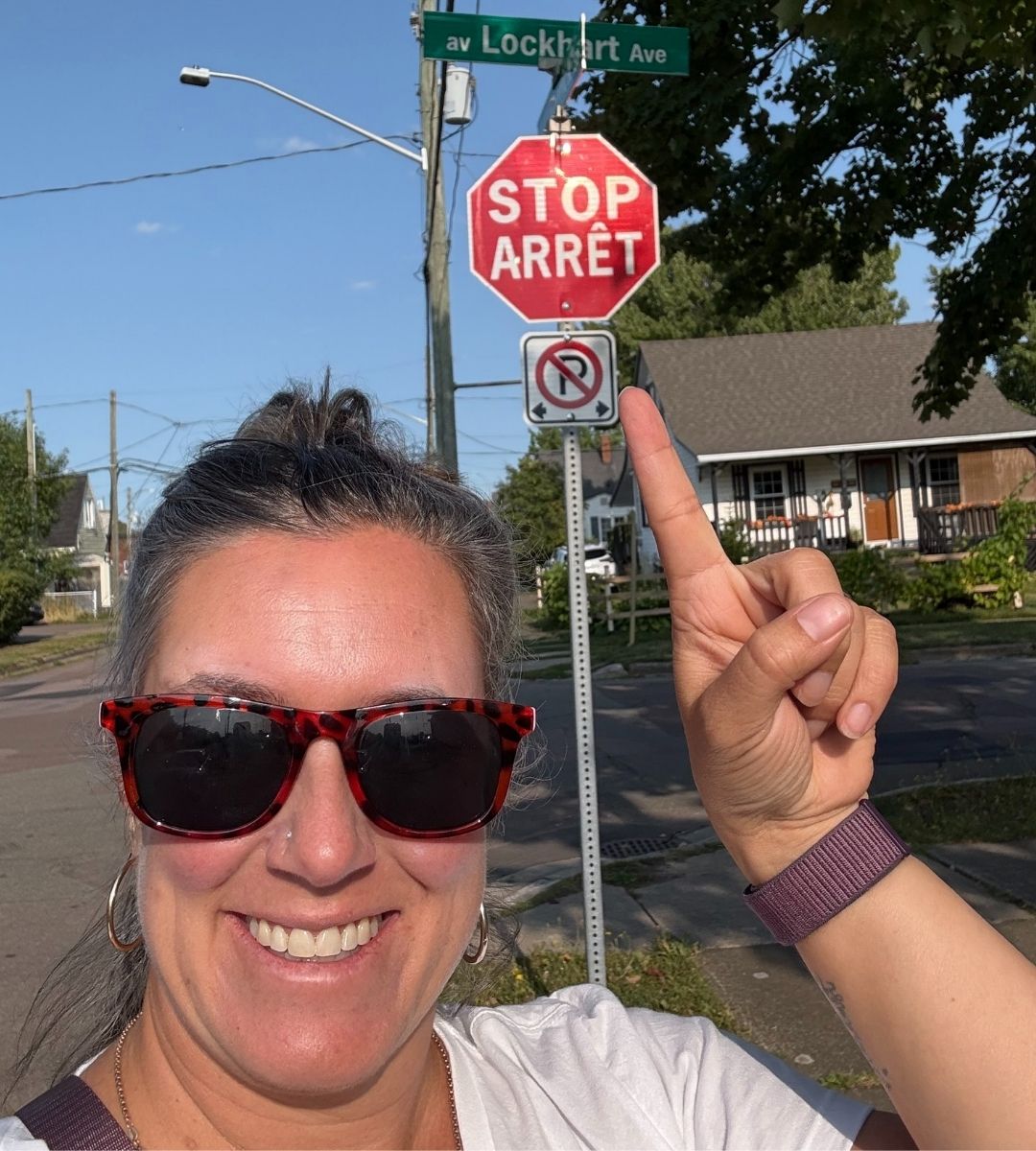 bilingual-stop-sign-maritimes Dominique pointing at a bilingual āStop / ArrĆŖtā sign in the Maritimes -highlighting the cultural connection to the Maritimes.